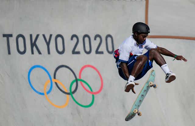 Man jumping off skateboard in mid-air in front of Tokyo 2020 sign