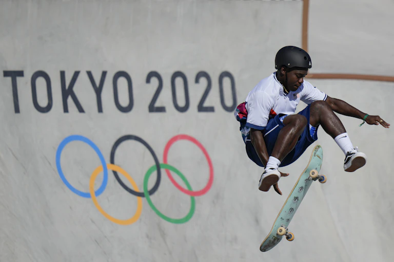 Man jumping off skateboard in mid-air in front of Tokyo 2020 sign