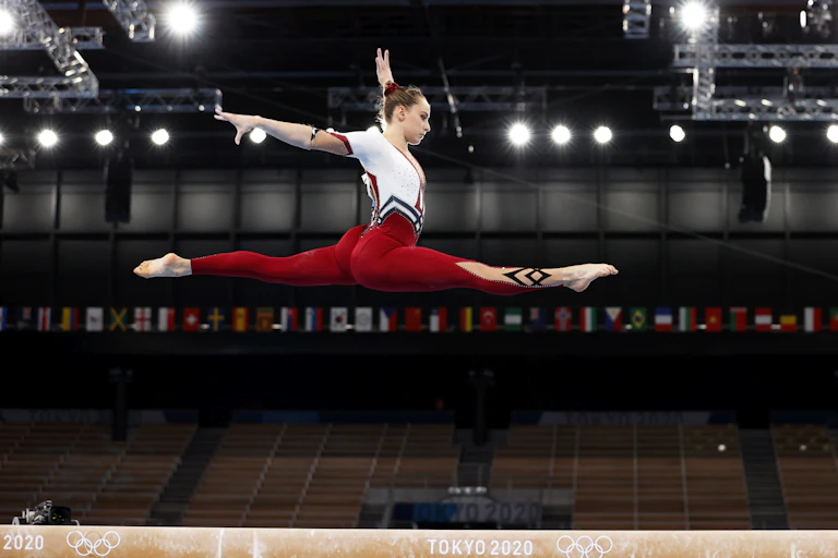 German gymnast Sarah Voss leaping high above the beam in a full-body red and white unitard rather than a revealing leotard.