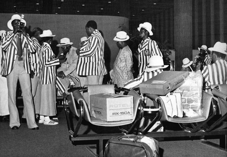 Crowd of men and women in matching striped jackets standing in airport gate.