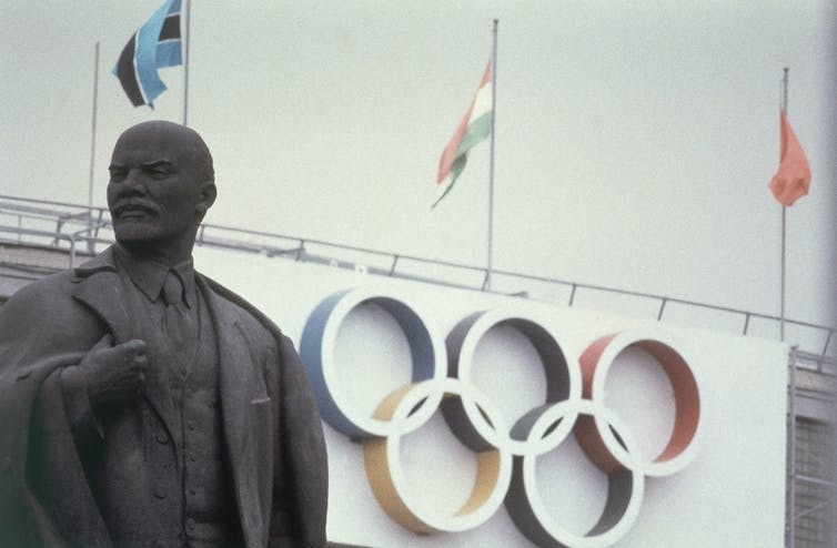 Statue of a man in front of a sports stadium bearing the Olympic rings