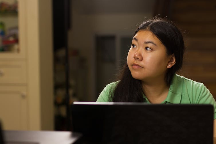 young woman looks away into the distance as she sits in front of a laptop