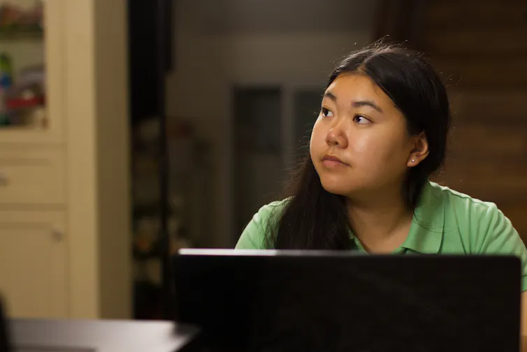 young woman looks away into the distance as she sits in front of a laptop