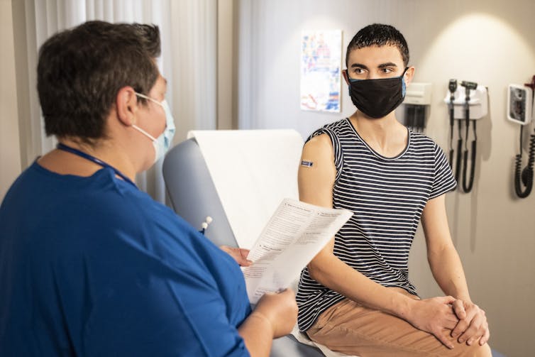 A health-care worker consults with a patient who appears to have just received a vaccination.
