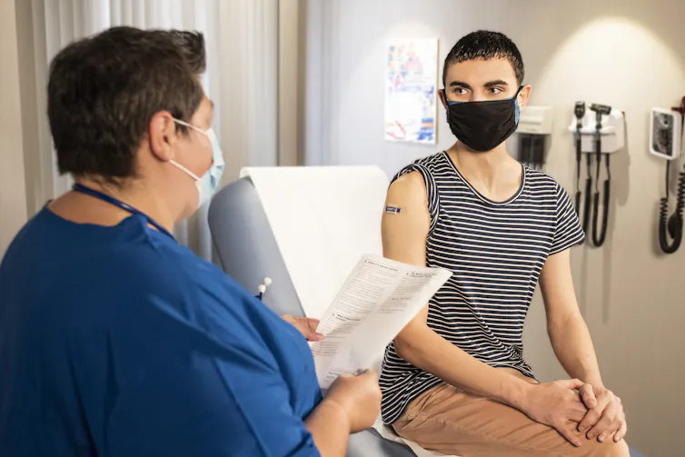 A health-care worker consults with a patient who appears to have just received a vaccination.