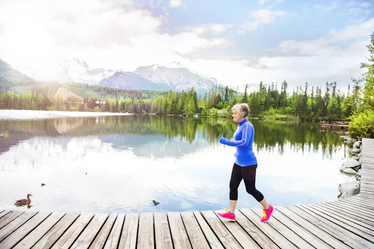 Older woman out for a jog on a pier by a lake.