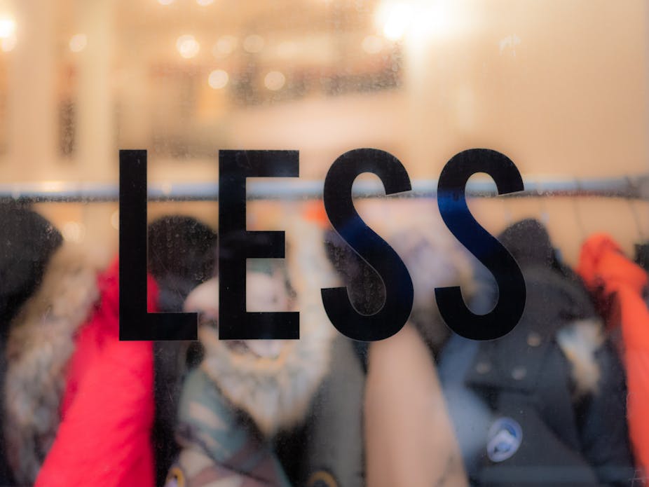 Clothes on a rack behind a window that says 'less'