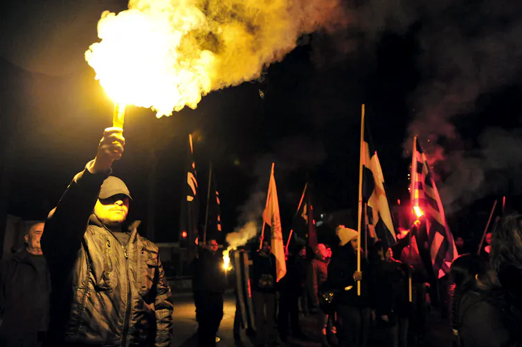 Protestors dressed in black wave flares at a night time gathering in Cyprus.