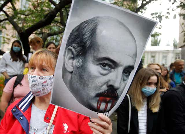 A protester holds a placard depicting Belarusian Lukashenko with blood dripping from his mouth