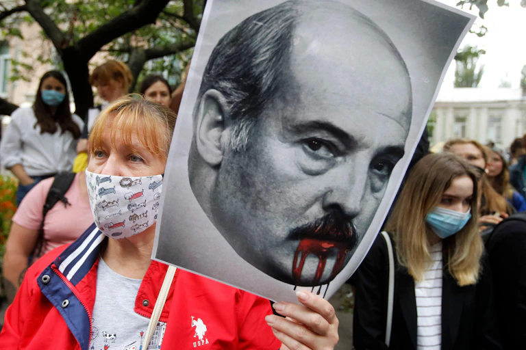 A protester holds a placard depicting Belarusian Lukashenko with blood dripping from his mouth