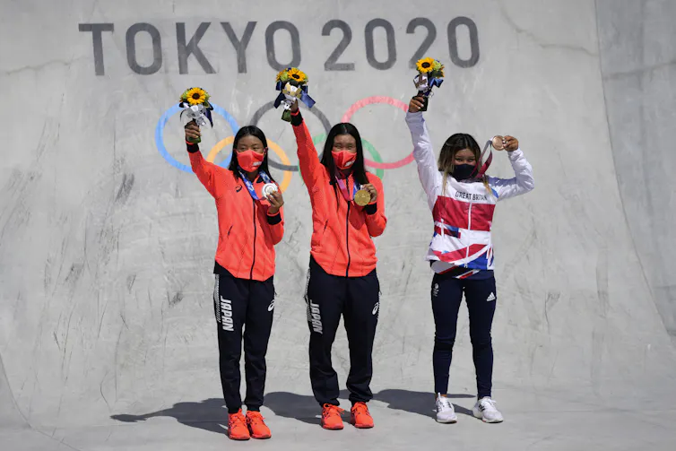 The three athletes wave as they stand in the skateboard park with the Tokyo 2020 sign behind them.