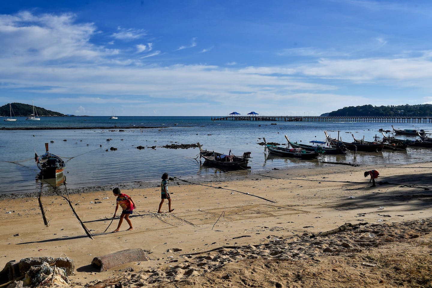 Moken children play on the beach, with small boats tied up in the shallows