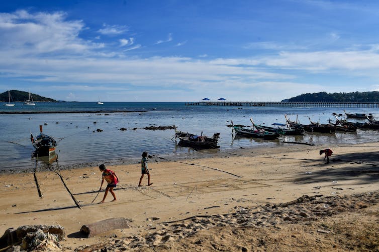 Moken children play on the beach, with small boats tied up in the shallows