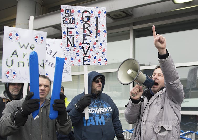 Striking workers hold signs as one speaks into a megaphone.