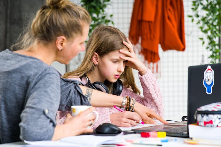 A mother helps her teenage daughter do homework during lockdown