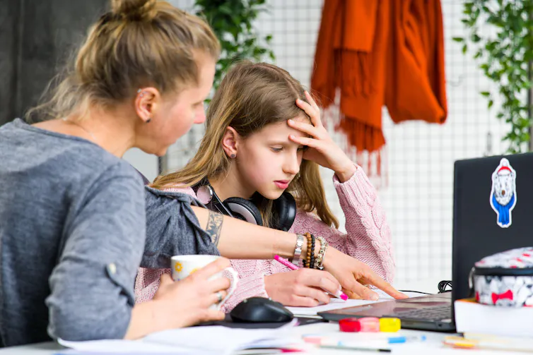 A mother helps her teenage daughter do homework during lockdown