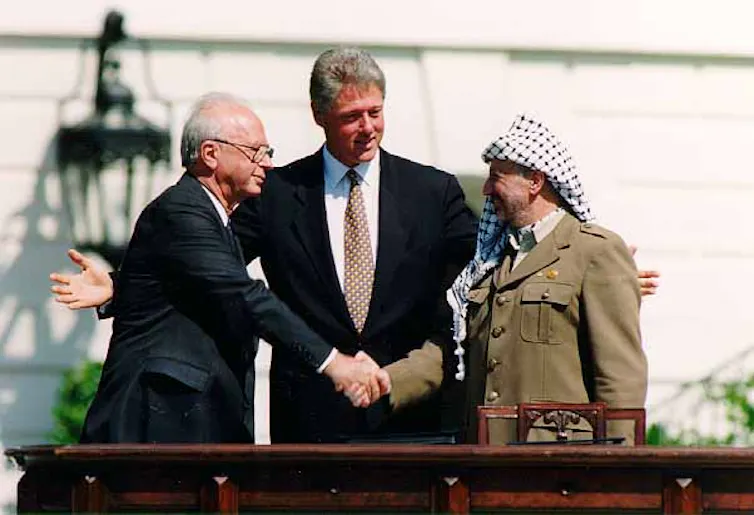 Israeli Prime Minister Yitzhak Rabin shaking the hand of PLO Chairman Yasser Arafat, with President Bill Clinton between them.