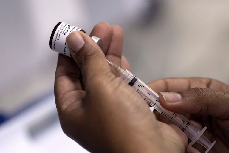 A hand prepares a vaccine from a vial.
