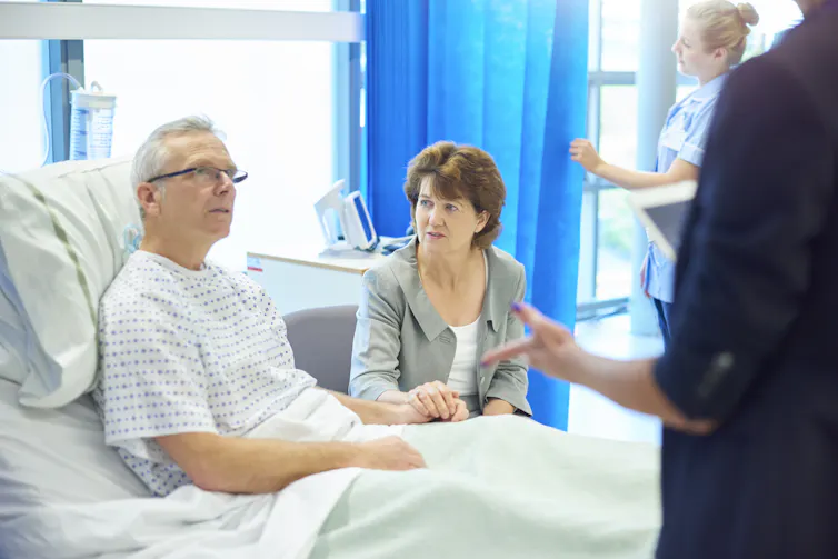 A patient in his hospital bed talks to his spouse and a doctor.