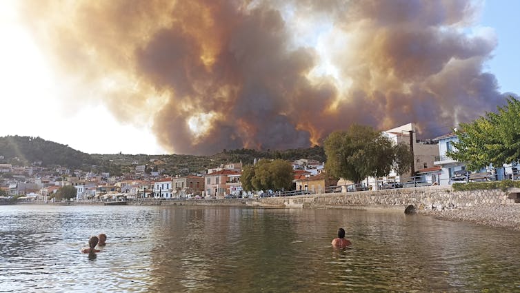 People swim in lake with bushfire smoke in the horizon