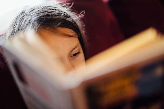 Close-up of young reader with book obscuring half their face