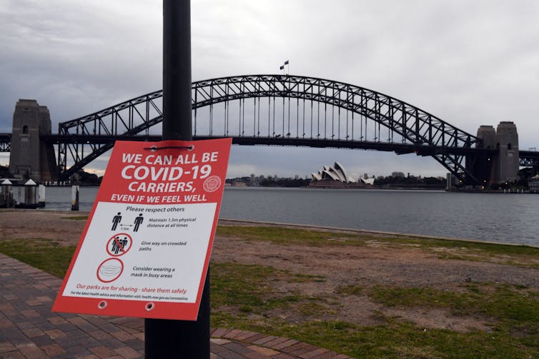 A sign about COVID in front of the Sydney Harbour Bridge