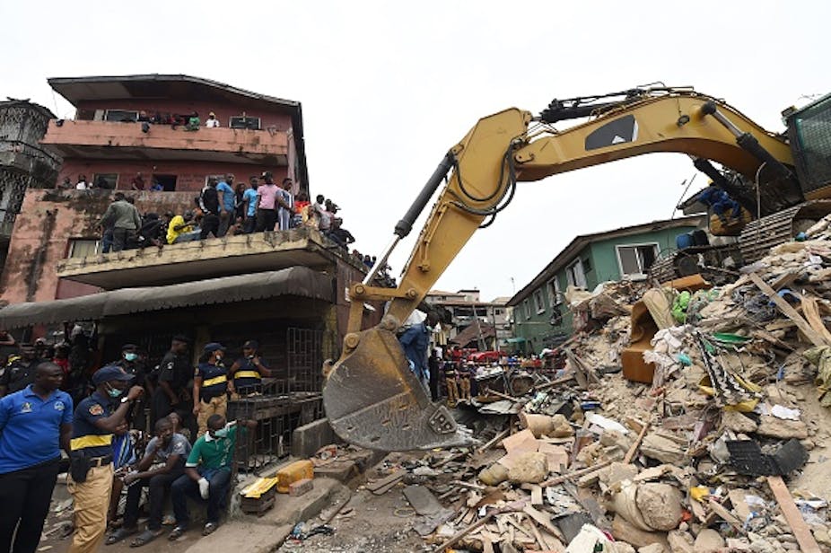 A bulldozer digging in rubble with people standing by and watching.