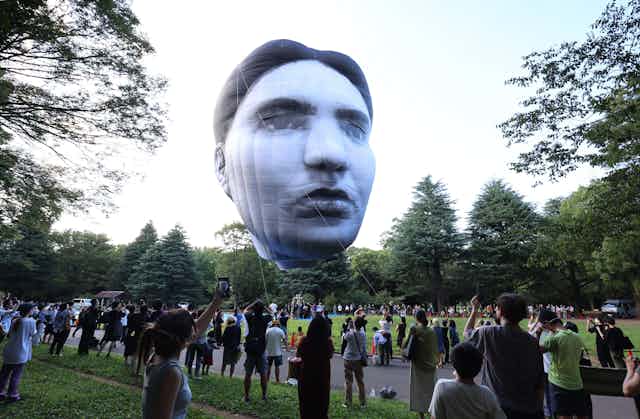A giant inflatable head hovers over a crowd of spectators in a Tokyo park