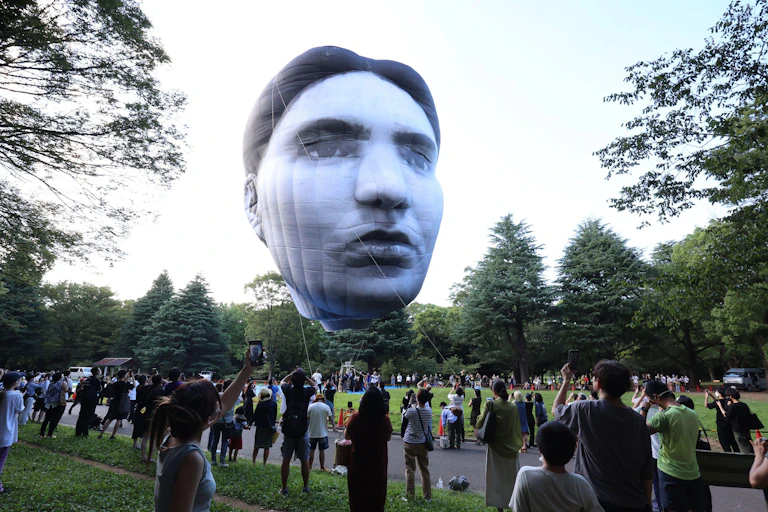 A giant inflatable head hovers over a crowd of spectators in a Tokyo park