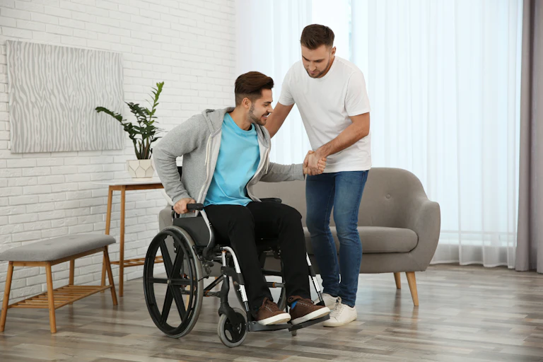 Man helping a wheelchair bound friend out of his wheelchair