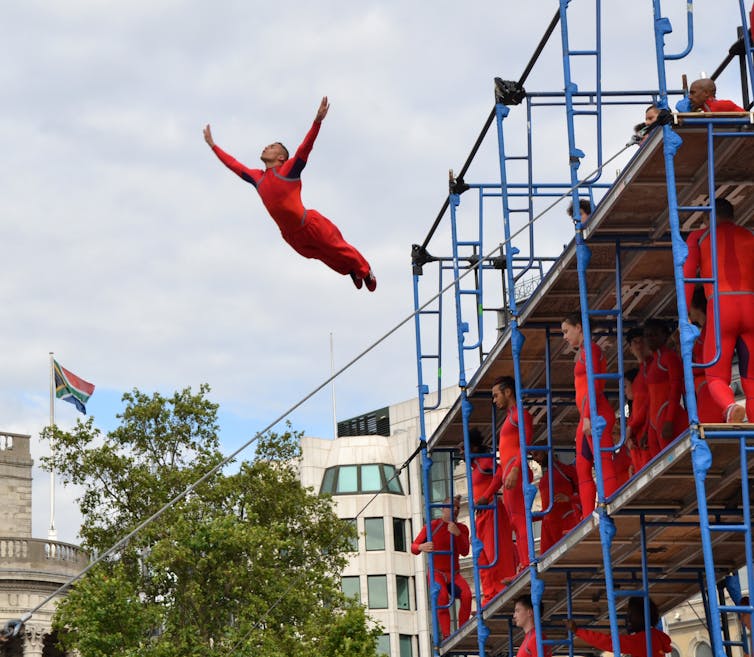 A dancer in a red unitard flies off a scaffolding structure in Central London