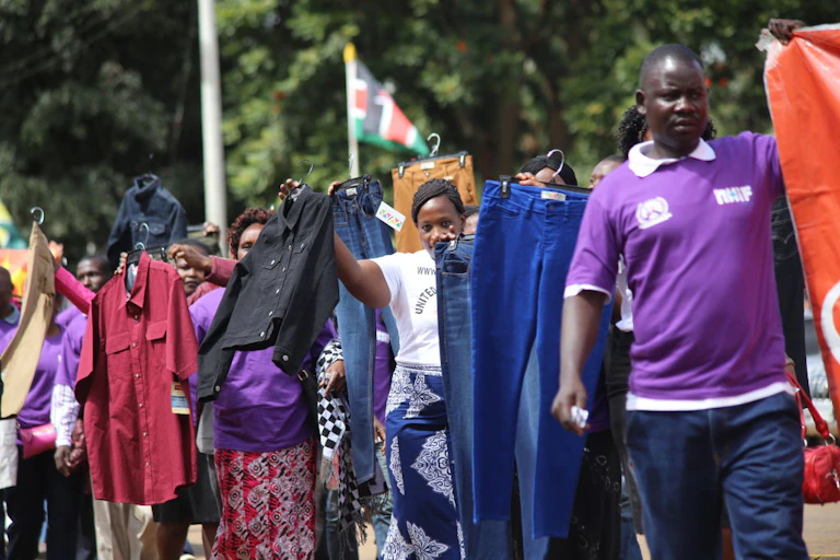 People walking outdoors hold up garments on hangers