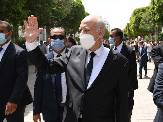 Tunisian president Kais Saied waving to supporters while flanked by security guards.