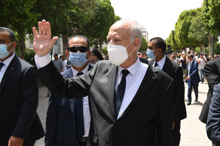 Tunisian president Kais Saied waving to supporters while flanked by security guards.