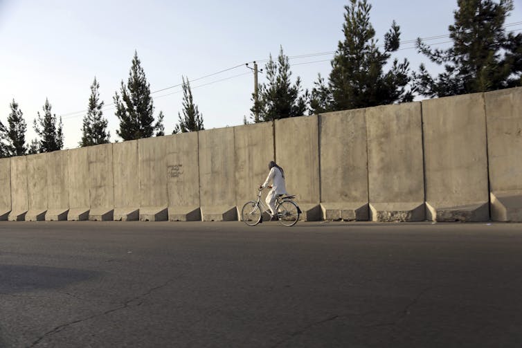 A man rides his bicycle walks past blast walls in Kabul.