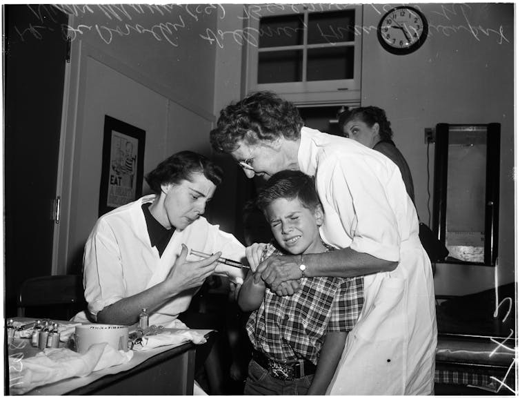 Nurse puts arm around boy as another nurse administers a polio vaccine shot