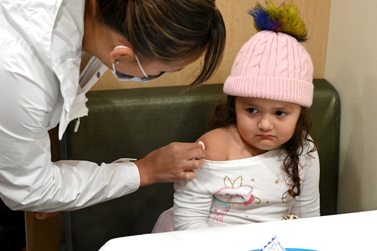 A toddler sits in chair with sleeve pulled down to receive flu shot