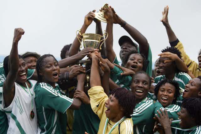 A crowd of women in football jerseys raise a trophy