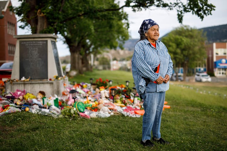 Senior woman stands beside a makeshift memorial of flowers and other offerings