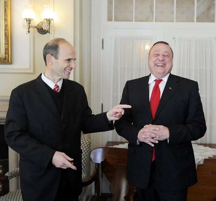 Two men in ties smiling.