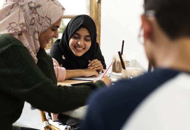 Two students wearing hijabs discuss and work together in a class.