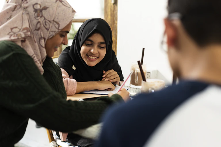 Two students wearing hijabs discuss and work together in a class.
