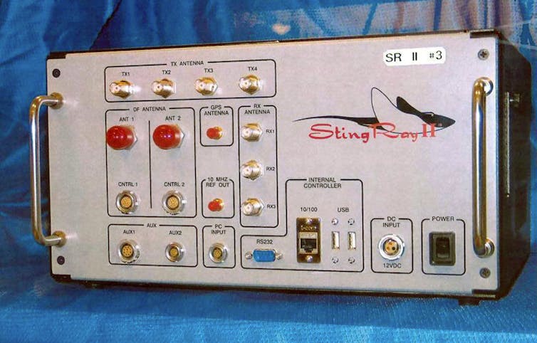 Um dispositivo eletrônico com alças em cada lado de um painel frontal contendo botões e luzes e uma representação gráfica de uma arraia