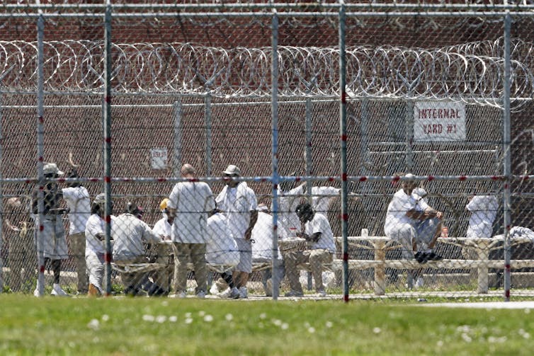 Prisoners populate a yard surrounded by razor wire.