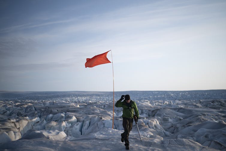 A person walks away from a red flag waving out on the ice.