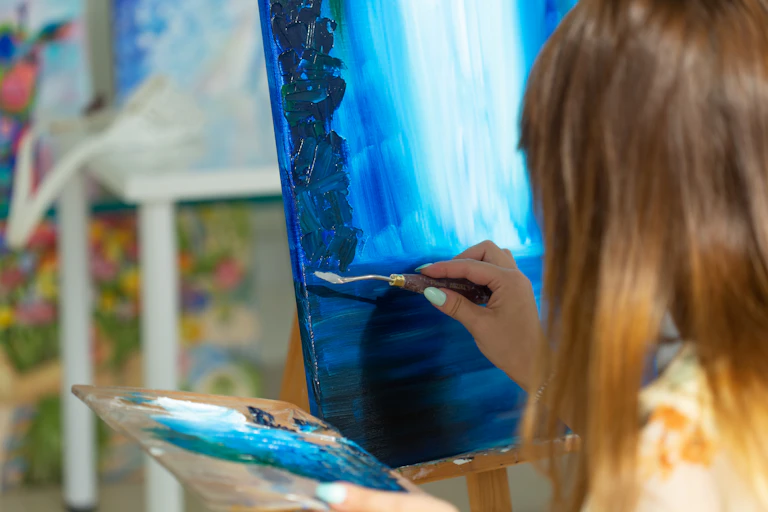 Girl painting in oil on canvas. Lots of blues of different hues.