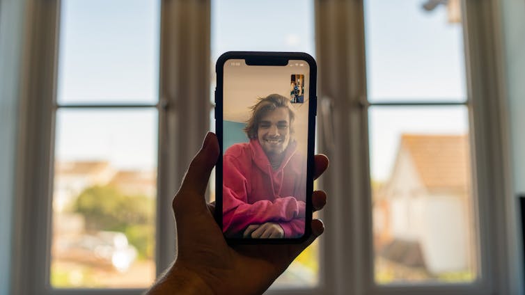 A hand holds up a smartphone on a video call.