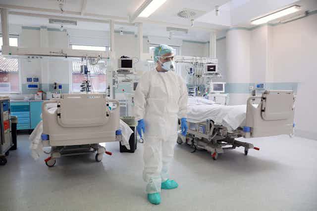 Medico in full PPE stands in front of two beds in an ICU.