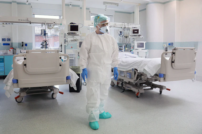 Medico in full PPE stands in front of two beds in an ICU.