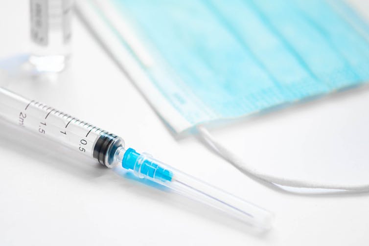 Syringe and mask on a white desk.